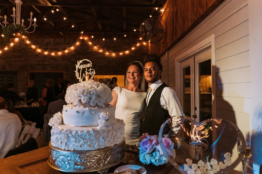 The bride and groom smile beside their tiered wedding cake during the reception at Masters Stables.