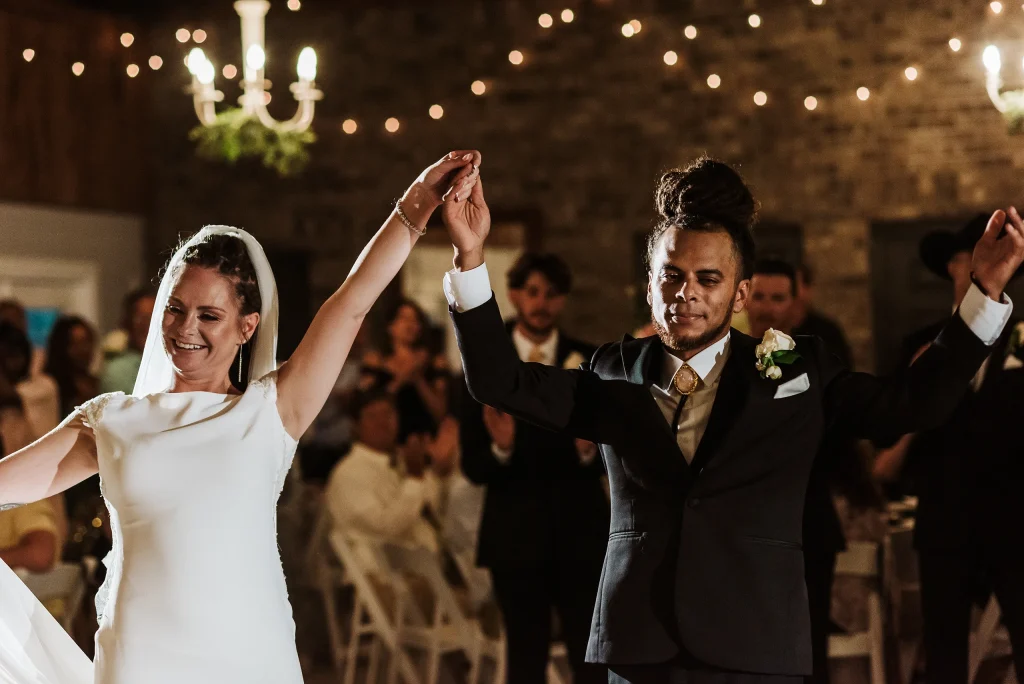 The bride and groom raise their joined hands in celebration during their first dance at Masters Stables.