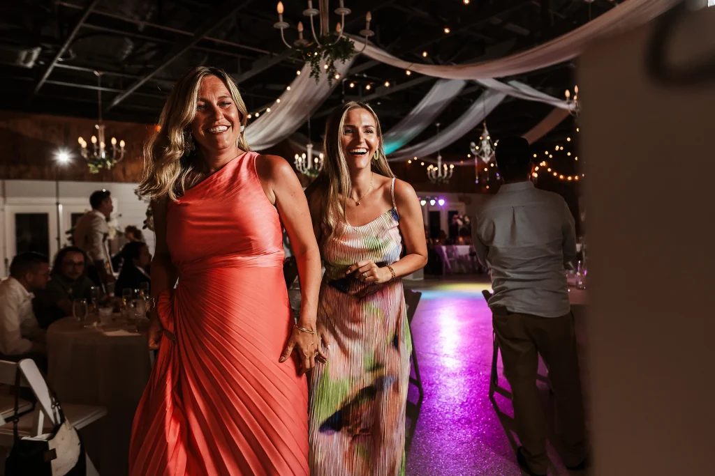 Two wedding guests laughing and dancing during the reception inside the decorated barn at Masters Stables.