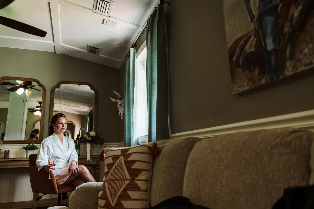 Bride sitting in the Masters Stables bridal suite with a glass of champagne, captured in a quiet moment before getting ready.