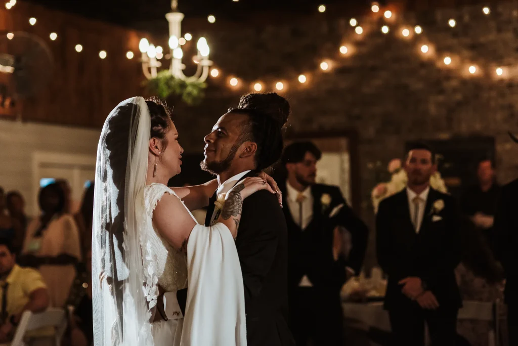 The bride and groom share a close, emotional moment during their first dance at Masters Stables, surrounded by warm string lights.