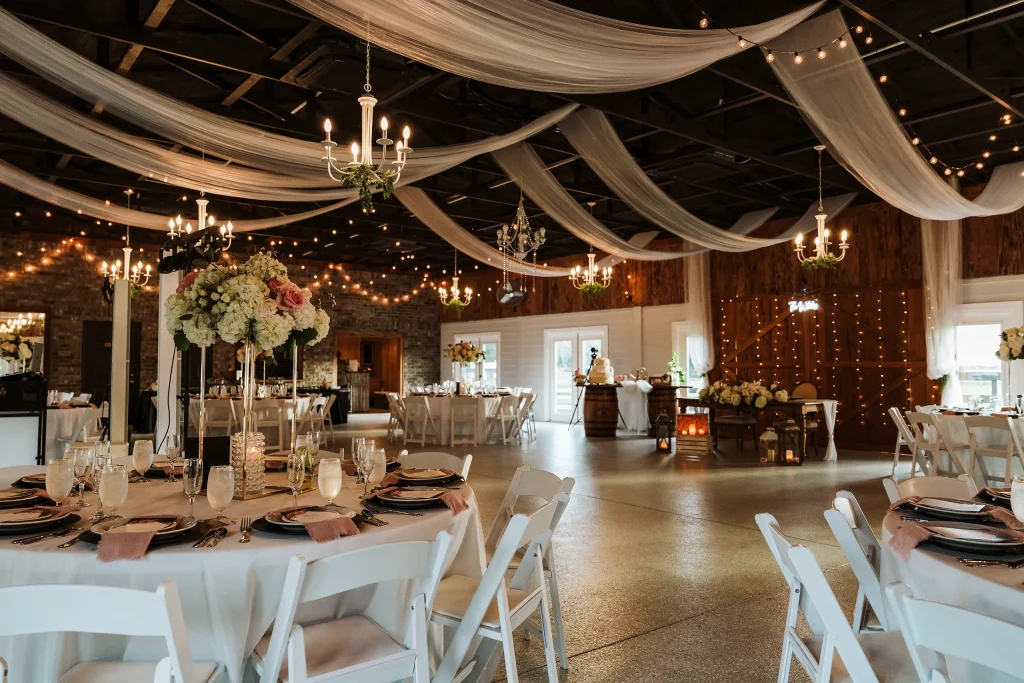 Elegant wedding reception setup at Masters Stables in Fellsmere, Florida, featuring ceiling drapery, chandeliers, floral centerpieces, and beautifully arranged guest tables.
