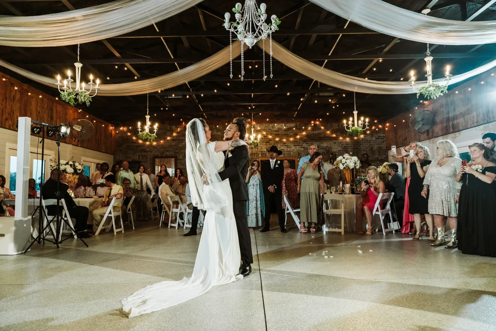 Bride and groom sharing their first dance at Masters Stables in Fellsmere, Florida, surrounded by guests inside the draped, chandelier-lit reception hall.